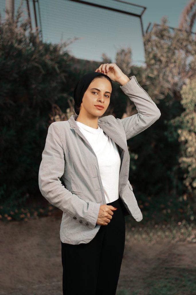 A confident woman poses outdoors in a stylish blazer and hijab, embodying modern fashion.